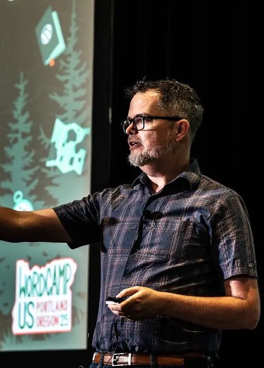 Matt Cromwell speaking on stage and pointing toward a slide.